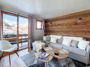 A modern living room with a sofa, a coffee table, and a chair. There is a large window with a view of mountains.
