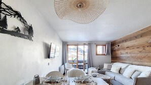 Un coin repas avec une table en bois dressée pour quatre personnes, un canapé et un téléviseur fixé au mur.