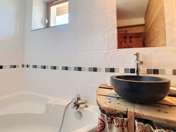 A bathroom with a bathtub, a wooden vanity with a large bowl sink, and a mirror above the sink.