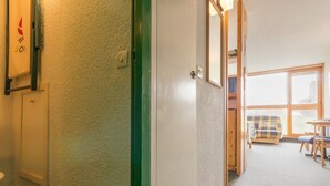Un couloir mène à une pièce dotée d’une grande fenêtre, d’une porte et d’une petite table avec une chaise.