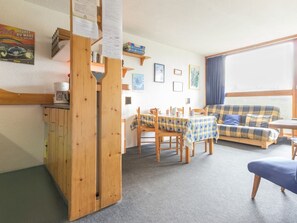 A cozy room with a wooden partition, a sofa, a dining table with chairs, and a coffee machine.