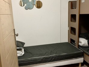 Een kleine kamer met een enkel bed, een houten deur en een spiegel aan de muur.