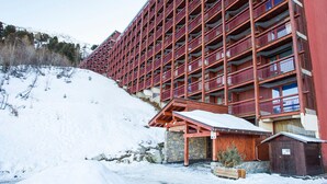 A multi-story hotel with a red exterior, located at the base of a snow-covered slope. - Cozy 3-room apartment, 6/7 pers, WiFi, near station (Les Arcs 2000)