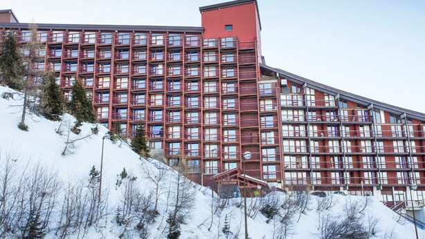 A large hotel with multiple floors, a prominent red section, and a snowy landscape with trees. - Cozy 3-room apartment, 6/7 pers, WiFi, near station (Les Arcs 2000)