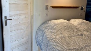 Un dormitorio con puerta de madera, una mesita de noche, una lámpara de pared y una cama con colcha a rayas.