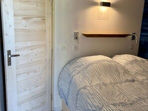 Ein Schlafzimmer mit Holztür, Nachttisch, Wandleuchte und einem Bett mit gestreifter Bettdecke.