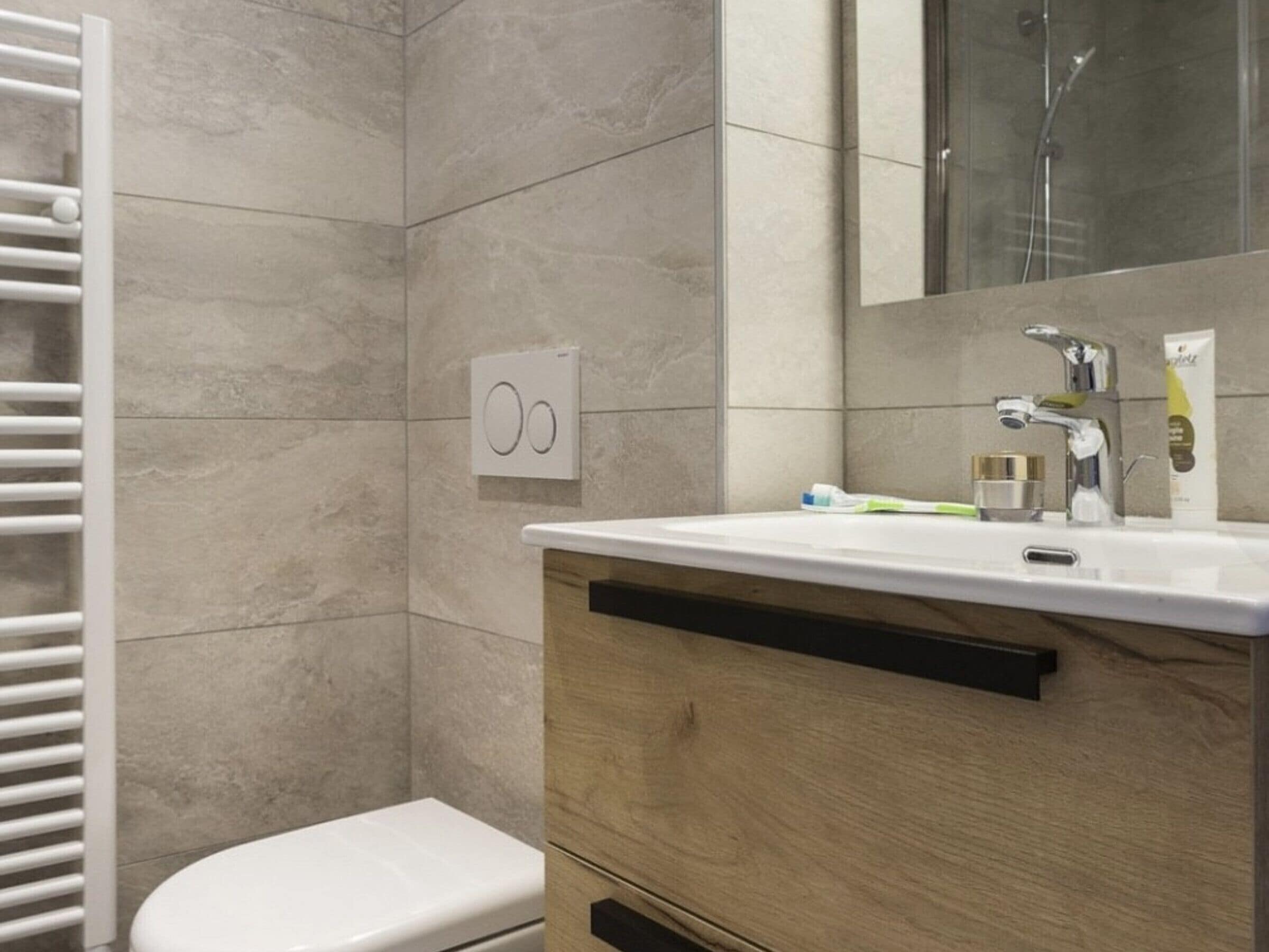 A modern bathroom with a white toilet, a wooden vanity with a mirror, and a shower area.