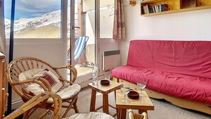 A cozy room with a red sofa, wicker chairs, a small table with glasses, and a bookshelf.