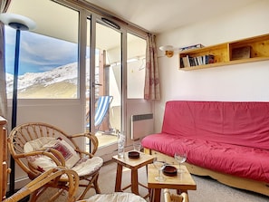 A cozy room with a red sofa, wicker chairs, a small table with glasses, and a bookshelf.