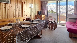 A dining area with a wooden paneled wall, a table set for four, and a view of mountains through a glass door.