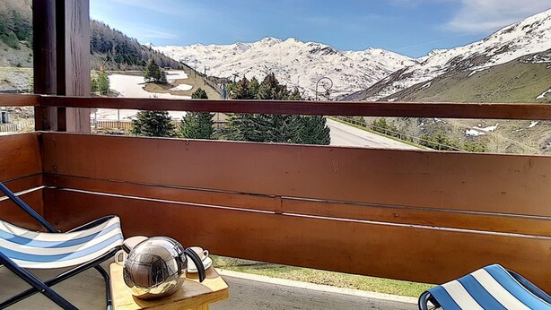 A balcony with two striped lounge chairs, a small wooden table with a metal object, and a view of snow-covered mountains.