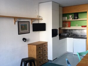 Une cuisine compacte avec des meubles blancs, un four à micro-ondes, une machine à café et un petit coin repas comprenant une table en bois et une seule chaise.