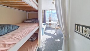 Quarto em dormitório com beliches, uma mesa pequena e vista para montanhas pela janela.
