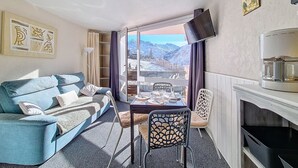 Uma sala de estar moderna com um sofá, uma mesa de jantar e vista para montanhas através de grandes janelas.