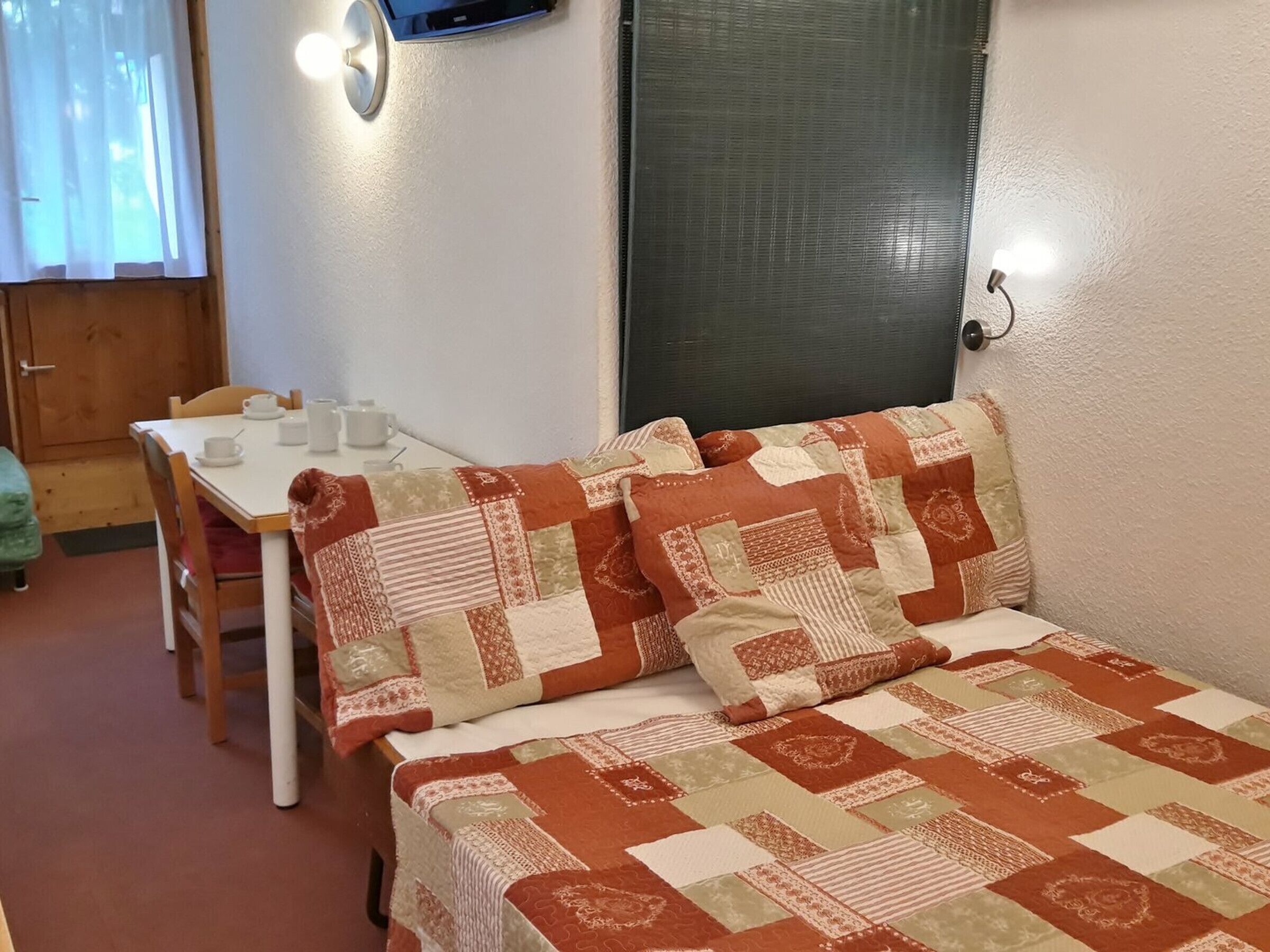 Une petite pièce agréable, avec un lit, une table sur laquelle se trouvent des tasses et une théière, et une fenêtre avec des rideaux.