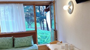 A room with a green sofa, a wooden table with white cups and a teapot, and a window with white curtains. - Cozy ski-in/ski-out studio with balcony (Les Arcs 1800)