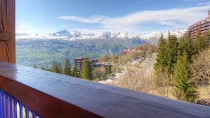A mountain view with snow-capped peaks, a wooden balcony, and buildings in the foreground.