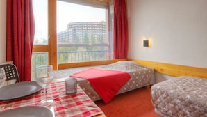 A hotel room with two beds, a dining table with plates and glasses, and a view of a building through the window.