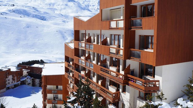 A modern multi-story hotel with wooden balconies and large windows, set against a snowy mountain backdrop. - Renovated studio at slopes, balcony, sleeps 4, Les Menuires (Les Menuires)