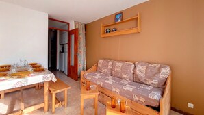 Een gezellige woonkamer met een bank, een eettafel gedekt met borden en glazen, en een keukenruimte zichtbaar door een open deur.