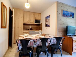 Un coin repas avec une table dressée pour quatre personnes, entourée de chaises, dans une pièce dotée de meubles en bois et d’un téléviseur posé sur un meuble en bois.