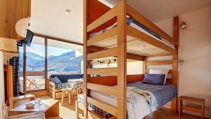 A cozy cabin with a bunk bed, a dining area with a table and chairs, and a large window offering a mountain view. - Bright studio with balcony on the slopes (Les Menuires)