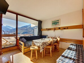 Een knus ingerichte kamer met een bank, een kleintje tafeltje en een bed. Er is een raam met uitzicht op bergen.
