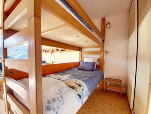 Een kleine kamer met een houten stapelbed, een tafeltje en een raam met uitzicht op een besneeerd landschap.