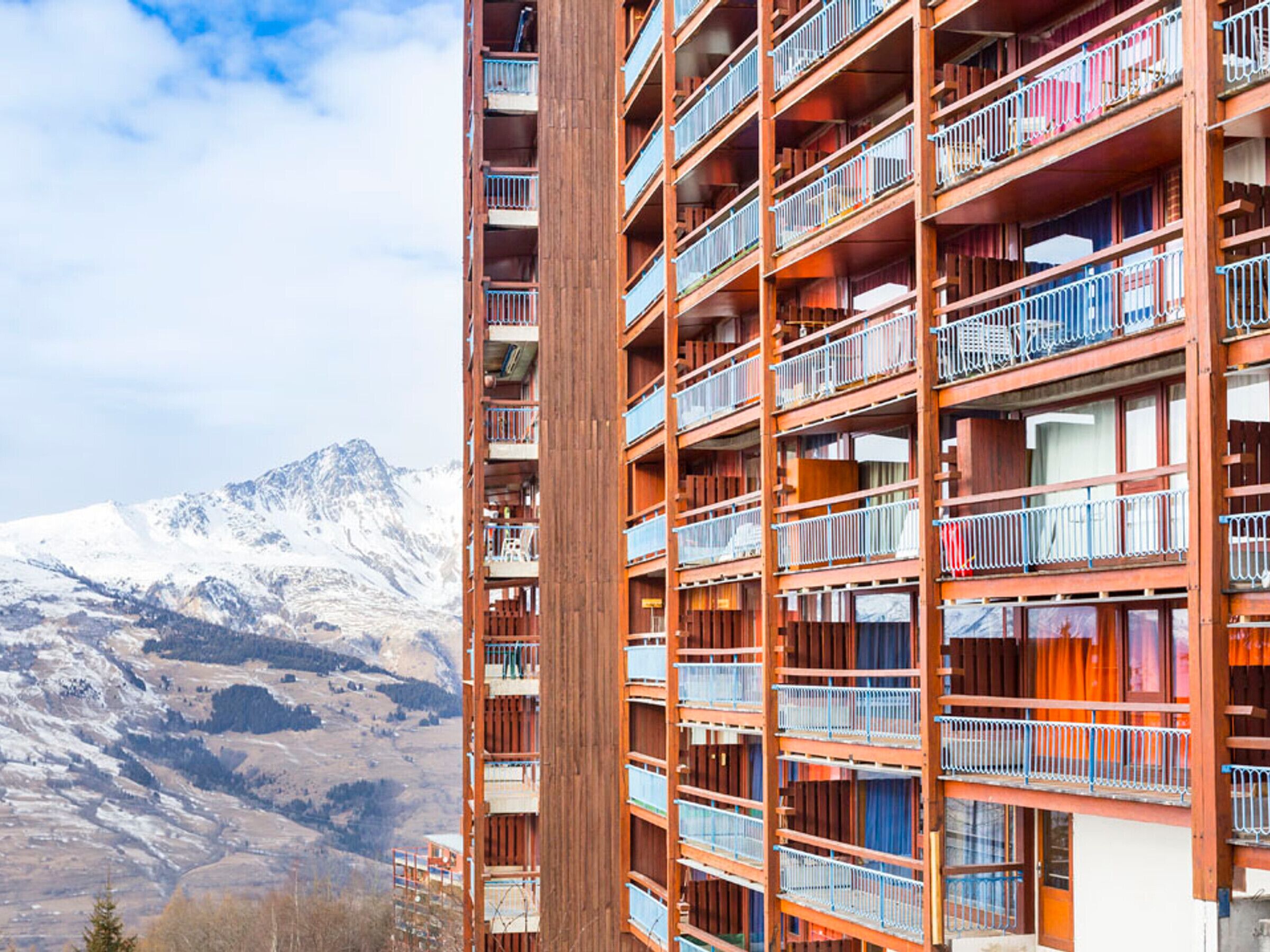 A multi-story hotel with balconies, set against a mountainous backdrop.