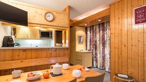 A wooden interior with a dining table set for breakfast, a microwave, and a clock on the wall. - 2-Room Apartment · Balcony · Free Wifi (Les Arcs 1800)