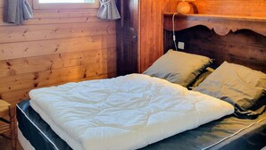 Ein Zimmer in einer Holzhütte mit einem Bett, Vorhängen, einer Lampe und einem Fenster.
