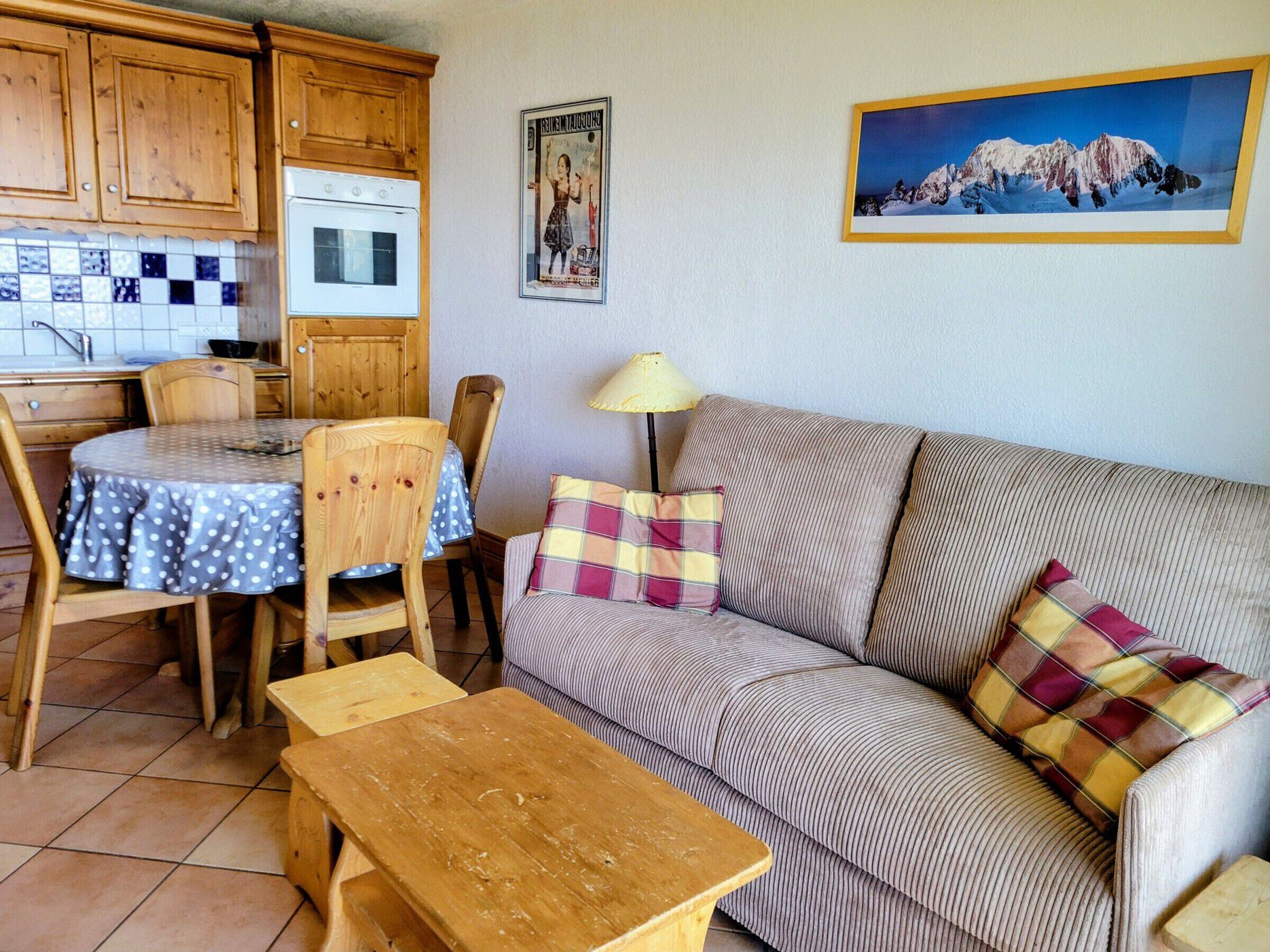 Ein gemütliches Wohnzimmer mit einer Couch, einem Esstisch, Stühlen, einer Lampe und einer Küchenzeile mit Holzschränken und einer gefliesten Spritzschutzwand.