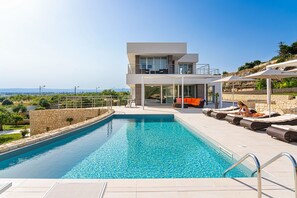 Una casa moderna de dos pisos con piscina, mobiliario exterior y vistas al paisaje.