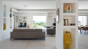 A modern living room with a grey sofa, a TV, and a view of the outdoors.