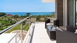 A balcony with a view of the sea, outdoor furniture, and a glass door leading to an interior space.