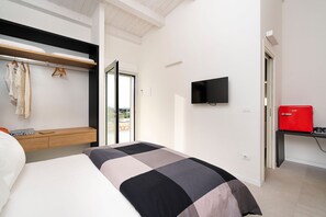 Una habitación de hotel moderna con una cama, un televisor, un minibar rojo y un balcón con vistas.