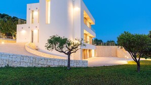 A modern two-story building with a curved facade, stone steps leading to the entrance, and a well-lit outdoor area.
