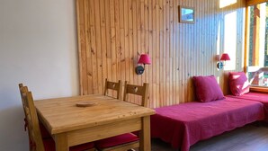 A room with a wooden table and chairs, a bed with red bedding, and a wall-mounted lamp. - Cozy Studio · Ski-In/Ski-Out · Balcony · Mountain Views (Les Arcs 1800)