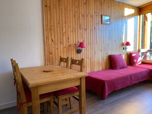Ein Zimmer mit Holztisch und -stühlen, einem Bett mit roter Bettwäsche und einer Wandleuchte.