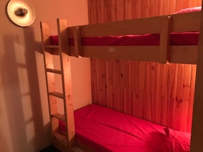 A bunk bed with a ladder, wooden panel walls, and a red bedspread.