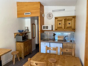 A compact kitchen with wooden cabinets, a microwave, a sink, and a dining area with a table and chairs. - Cozy Studio · Ski-In/Ski-Out · Balcony · Mountain Views (Les Arcs 1800)