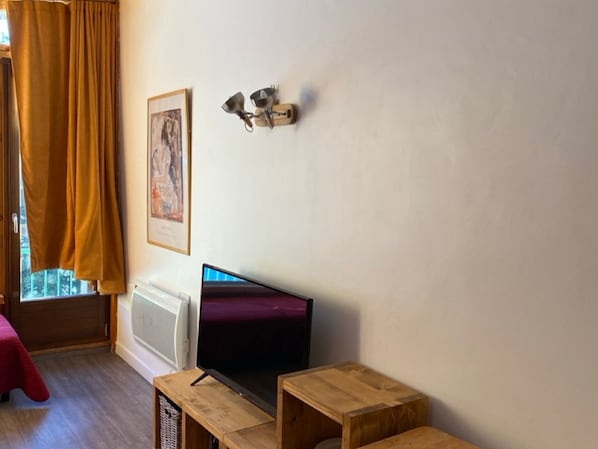 A room with a television, a framed picture on the wall, and a window with curtains.