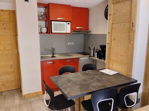 Une cuisine compacte équipée d’un four à micro-ondes, d’un évier et d’un petit réfrigérateur. On y trouve également une table à manger avec quatre chaises et une machine à café.