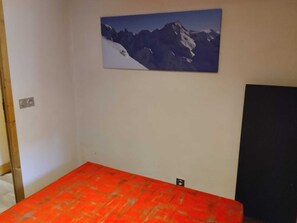 Ein Zimmer mit einem Bett, einem Bergpanorama und einem schwarzen Gegenstand an der Wand.