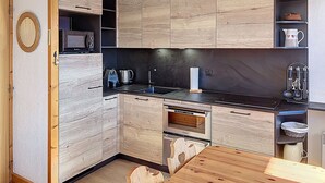 A compact kitchen with wooden cabinetry, a built-in microwave, a gas stove, and a hanging pendant light.