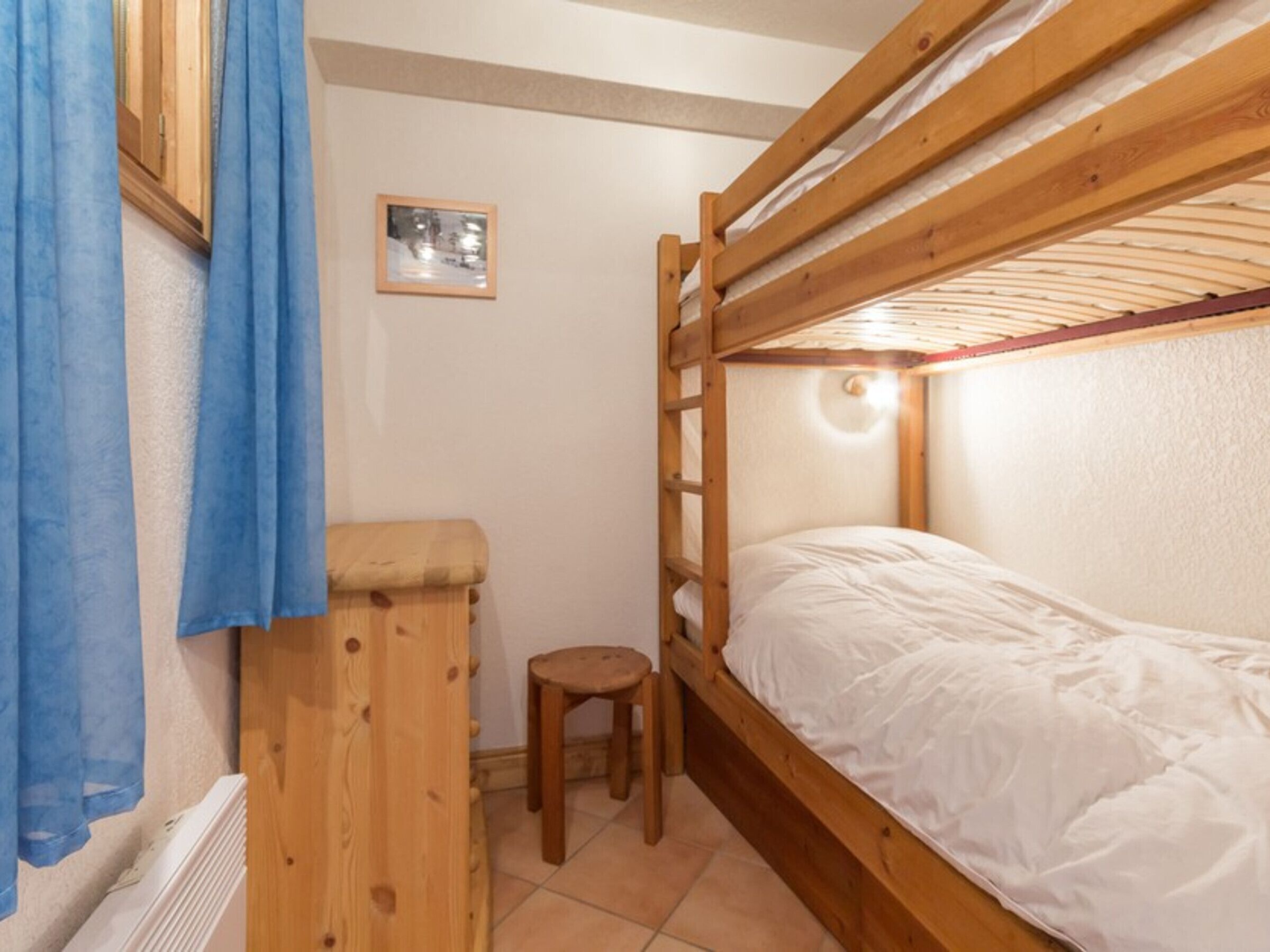 A bunk bed room with a wooden ladder, a small stool, and a framed picture on the wall.