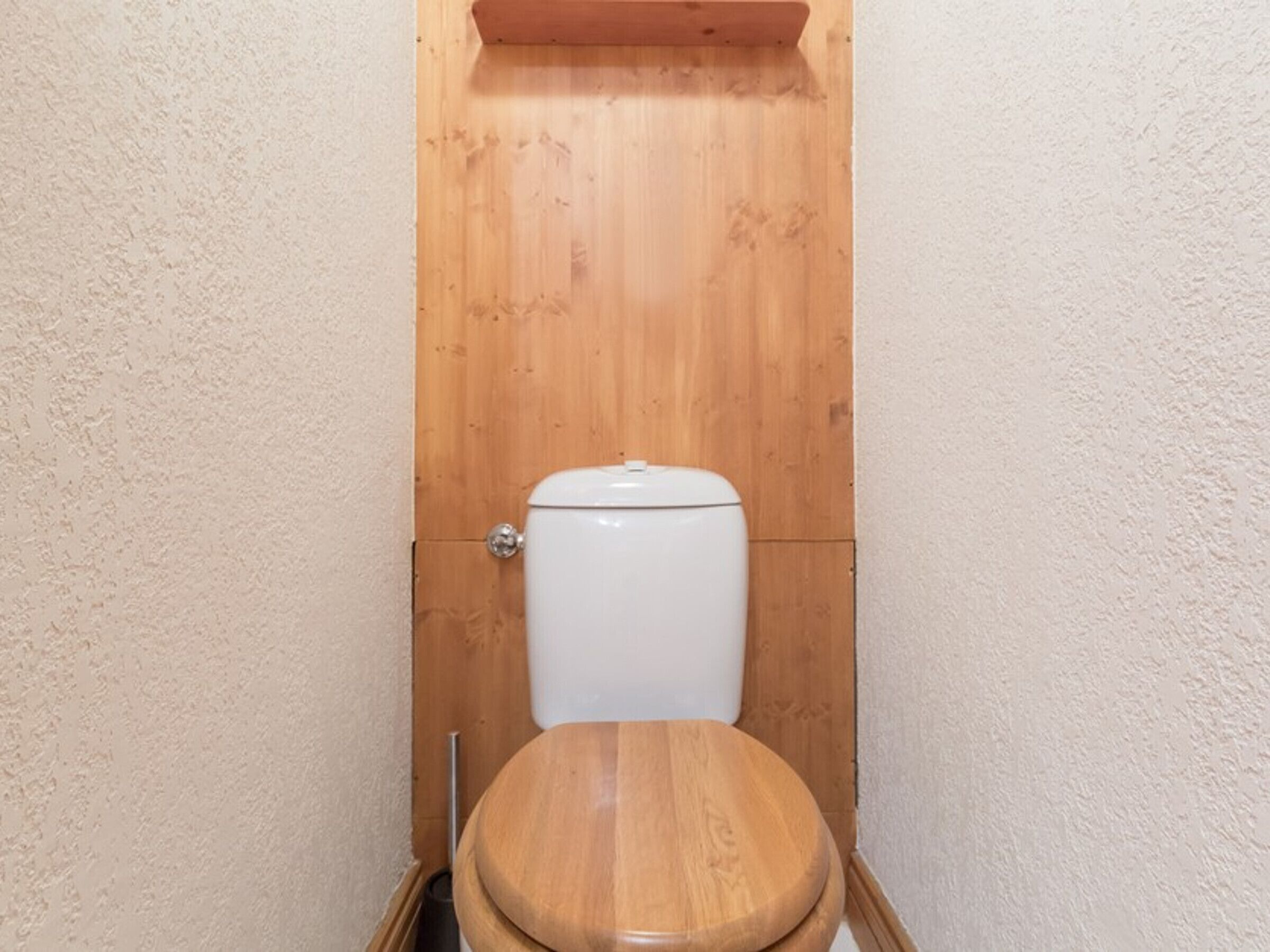 Een kleine badkamer met houten kozijnen, een wit toilet en een houten zitje.