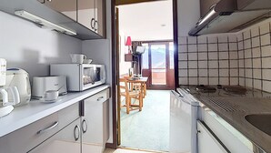 A compact kitchen with a microwave, coffee maker, and a stove. There is a dining area with a table and chairs visible through an open door. - Studio at the Foot of the Slopes · South Balcony (Les Menuires)