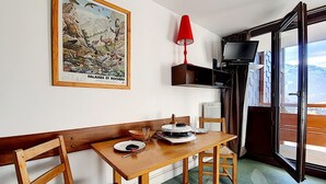 A dining area with a wooden table, chairs, a red lamp, and a framed picture on the wall. - Studio at the Foot of the Slopes · South Balcony (Les Menuires)