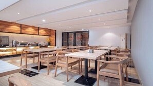 A modern dining area with wooden tables and chairs, a kitchen in the background, and a clean, minimalist design. - Nanning Unitour Hotel (Nanning)